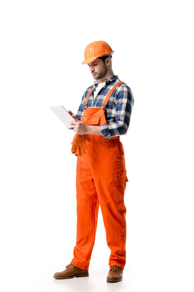 Young repairman in orange overall and hard hat using digital tablet isolated on white
