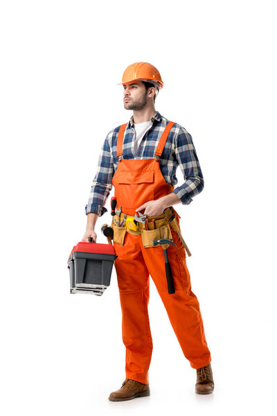 Young confident repairman in orange overall holding tool box isolated on white