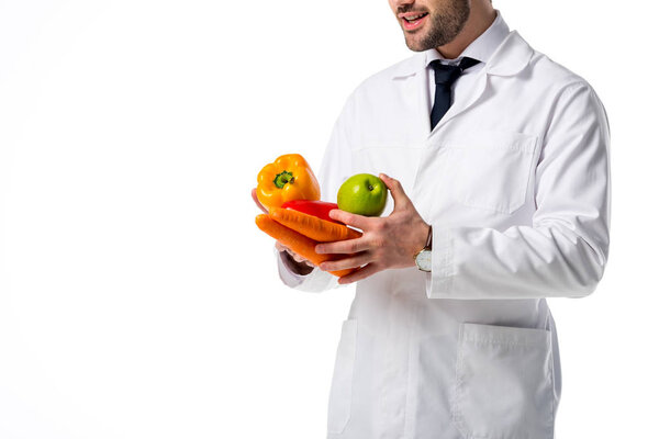 cropped shot of nutritionist in white coat with fresh vegetables and apple in hands isolated on white