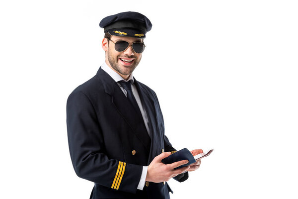 smiling pilot in uniform and sunglasses wit passport and ticket isolated on white
