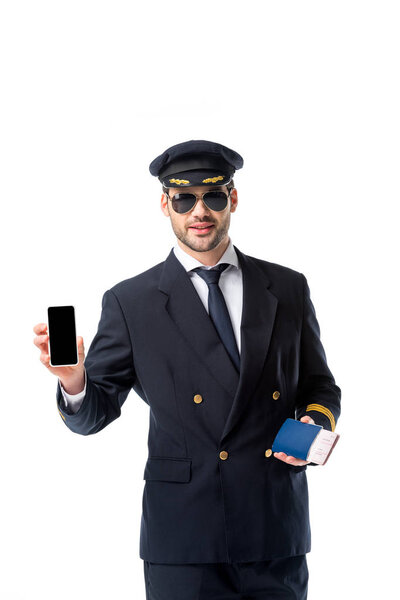 portrait of pilot in uniform with passport and ticket in hand showing smartphone with blank screen isolated on white