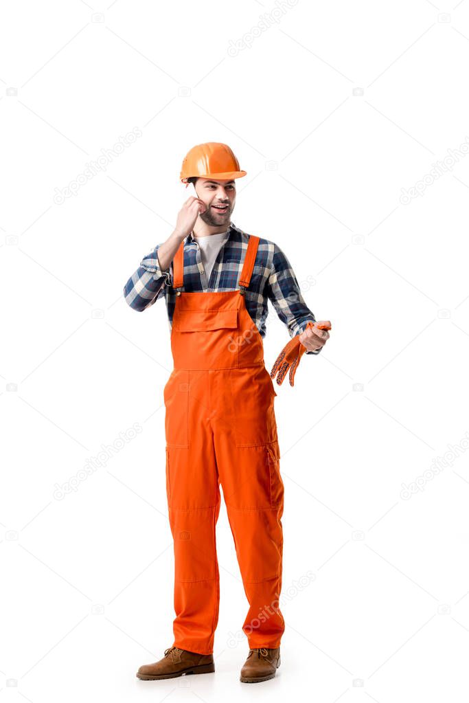 Young repairman in orange overall and hard hat talking on the phone isolated on white