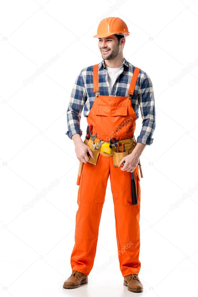 Smiling builder in orange overall and tool belt isolated on white