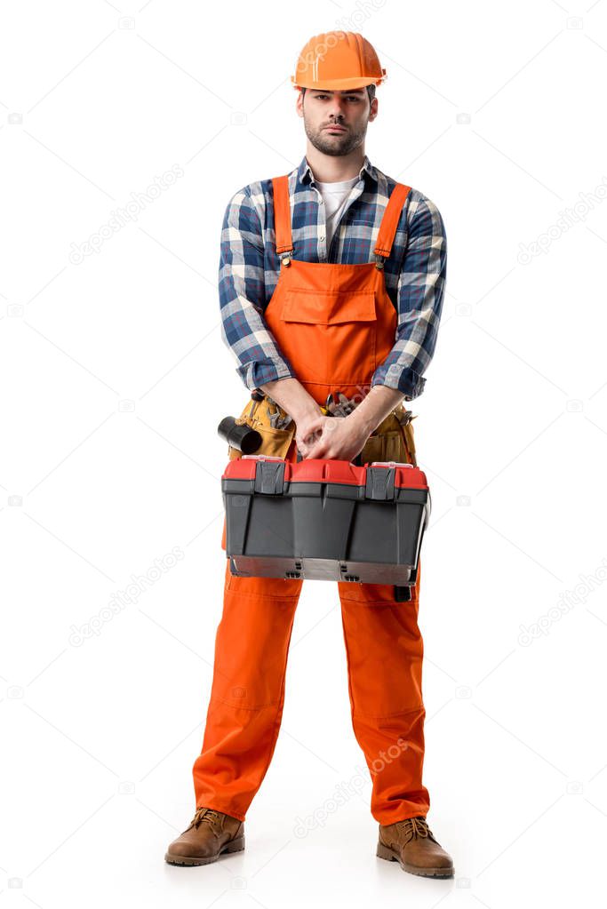 Confident handyman in orange overall and hard hat holding tool box isolated on white