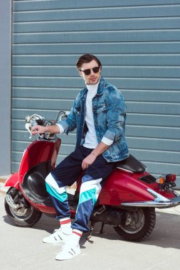young man in stylish vintage clothes sitting on scooter clipart