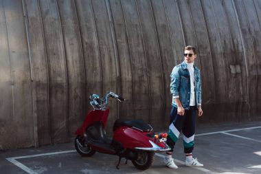 stylish young man in stylish denim jacket with vintage scooter on parking clipart