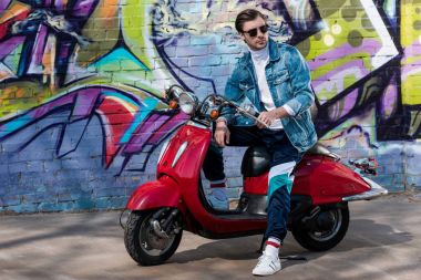 tuğla duvar grafiti ile önünde vintage kırmızı scooter üzerinde şık genç adam