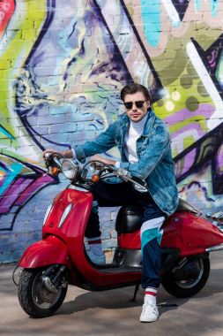 tuğla duvar grafiti ile önünde vintage kırmızı scooter üzerinde çekici bir genç adam