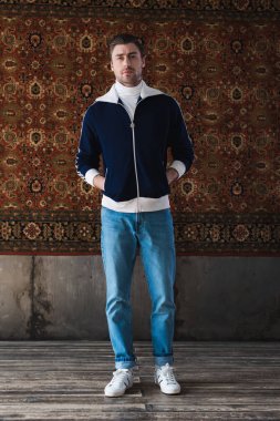 duvarda asılı halı önünde şık giysiler içinde ciddi genç adam