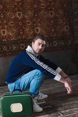 duvarda asılı halı önünde vintage küçük bavul oturma ağız kavgası ile genç adam