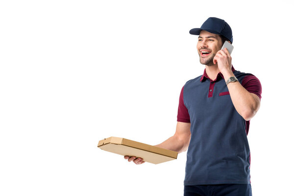 portrait of smiling delivery man with cardboard pizza box talking on smartphone isolated on white