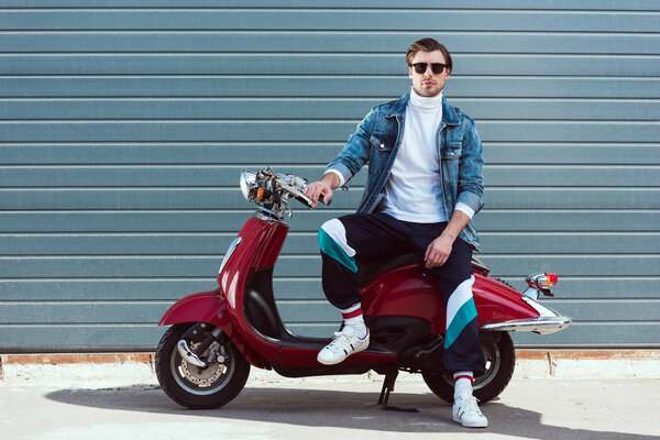 Красивый молодой человек в стильной старой школьной одежде на винтажном красном скутере
