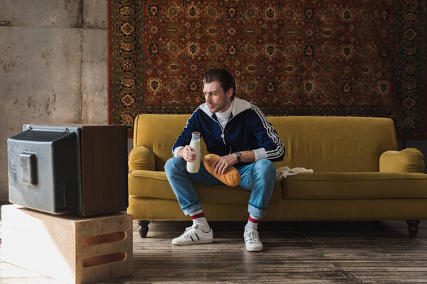 handsome young man in vintage clothes with bottle of milk and loaf of bread watching tv