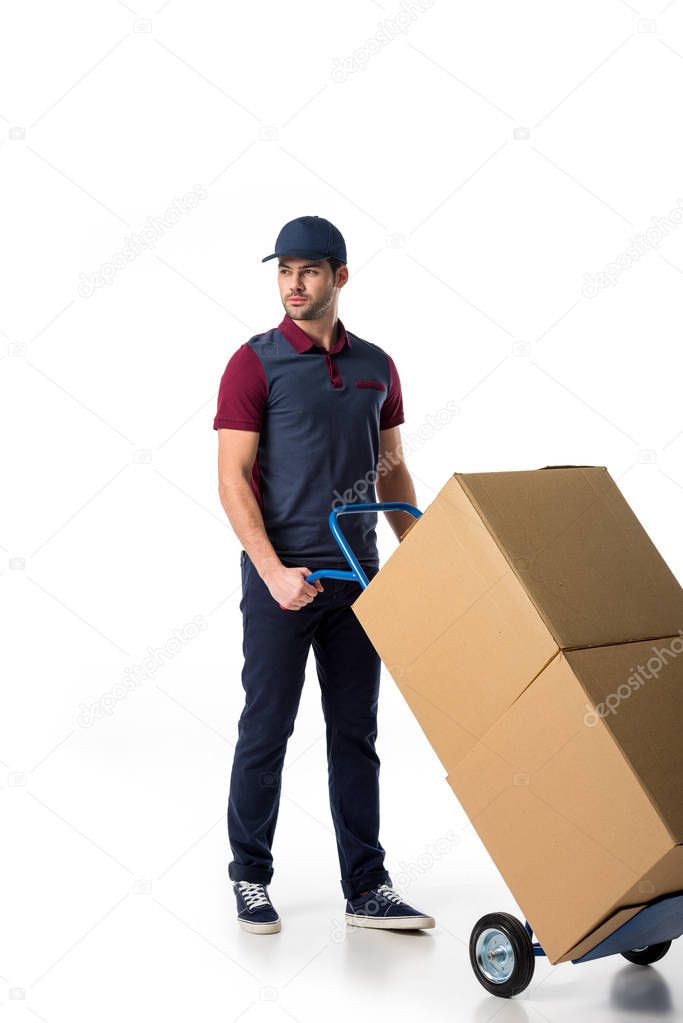 delivery man in uniform pushing hand truck with cardboard boxes isolated on white
