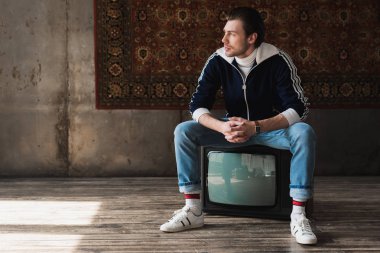 vintage giyim retro TV'nin önünde duvara asılı halı üzerinde oturan düşünceli genç adam
