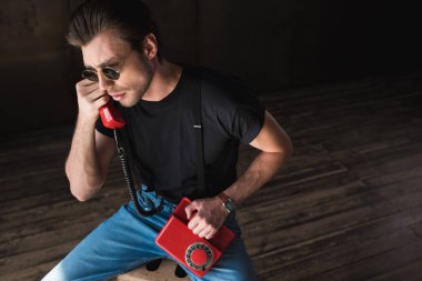 yakışıklı genç siyah tişört ve pantolon askısı retro kablolu kırmızı telefonla konuşurken, yüksek açılı görünüş