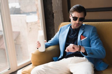 şişe süt ile kanepede oturan ve bakarak şık elbiseli çekici genç adam