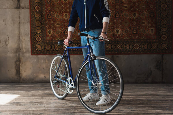 cropped shot of man in vintage clothes with road bike in front of rug hanging on wall