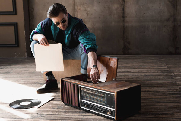 handsome nostalgic man in vintage windcheater with vinyl record player
