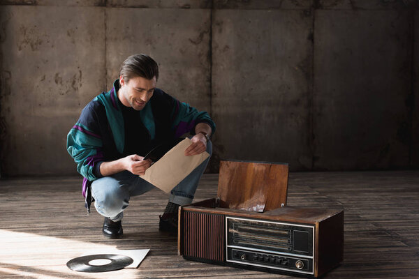 happy nostalgic young man in vintage windcheater with vinyl record player