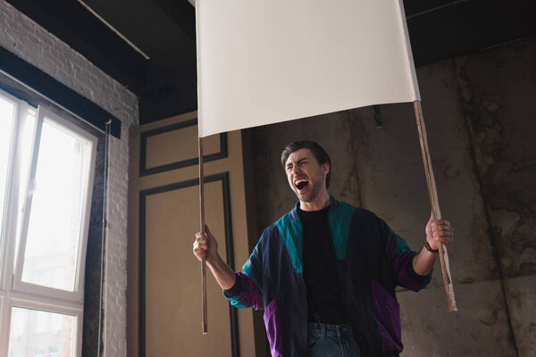 bottom view of angry shouting young man in vintage windcheater with blank placard