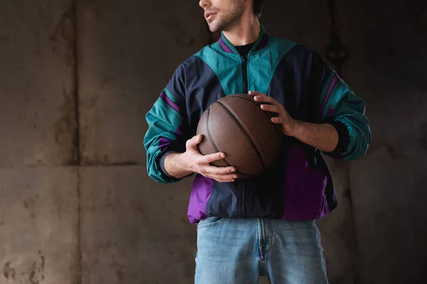 cropped shot of young man in vintage windcheater with basketball ball