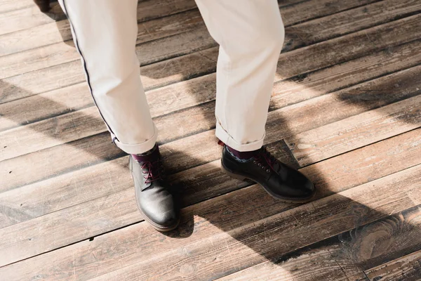 穿着时髦的鞋子和裤子站在简陋的木地板上的人的裁剪镜头 — 图库照片