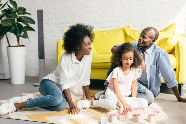 アフリカ系アメリカ人の両親と家の床に木製のブロックを一緒と遊ぶ娘  — 無料ストックフォト