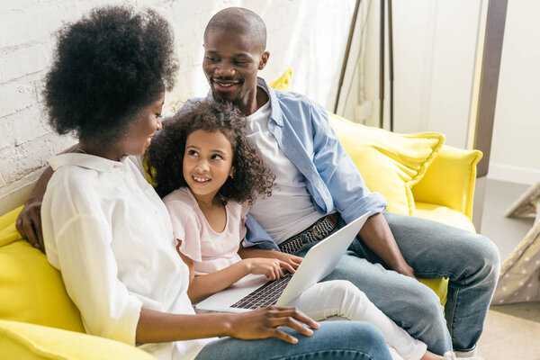 Африканская американская семья с ноутбуком, лежащим на диване вместе дома
