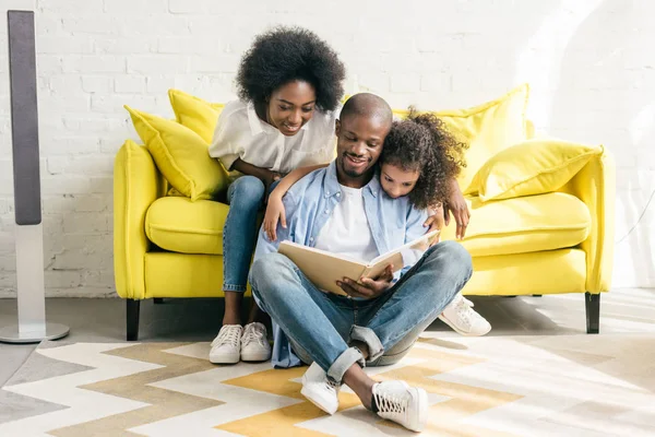 アフリカ系アメリカ人の両親と小さな娘本を読んで一緒に家庭で笑顔 — ストック写真