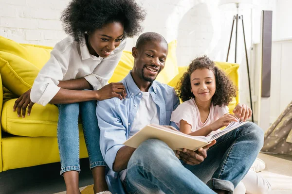 Padres Afroamericanos Felices Pequeña Hija Leyendo Libro Juntos Casa —  Fotos de Stock