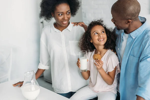 Усміхнена Афроамериканська Дитина Склянкою Молока Печиво Руках Батьки Біля Кухні — стокове фото
