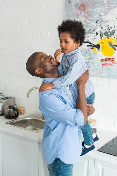 Afro Americano Homem Segurando Pequeno Filho Com Biscoito Cozinha Casa — Fotografia de Stock