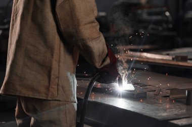 cropped shot of of manufacture worker welding metal with sparks at factory  clipart