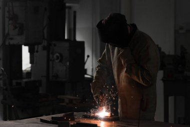 front view of worker in protection mask welding metal at factory  clipart