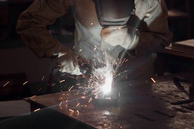 front view of welder in protection mask working with metal at factory  clipart