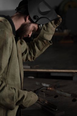 onun iş yerinde bakmak için koruyucu maske kaldırma Kaynakçı yan görünüm 