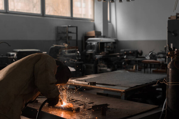 manufacture worker welding metal with sparks at factory 