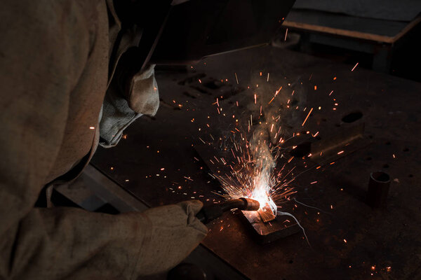 обрезанное изображение работника в защитной маске сварки металла на заводе
 