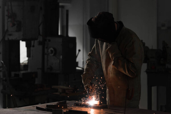 front view of worker in protection mask welding metal at factory 