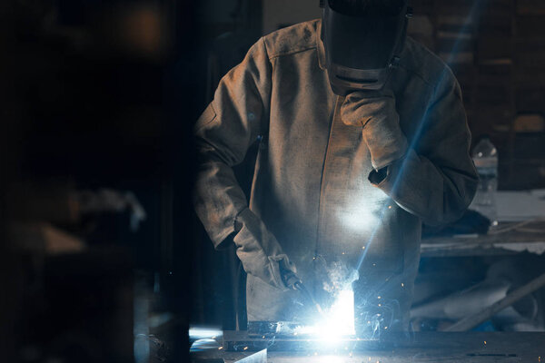 welder in protection mask working with metal at factory 