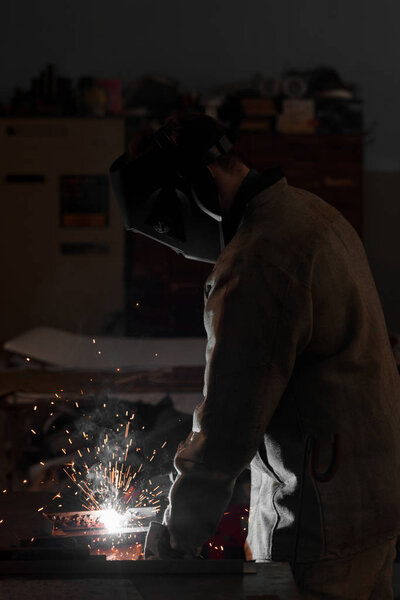 side view of manufacture worker welding metal with sparks at factory 