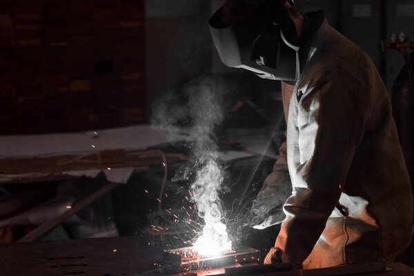 welder in protection mask working with metal at factory 