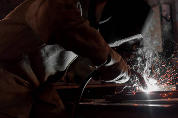 cropped image of manufacture worker welding metal with sparks at factory 