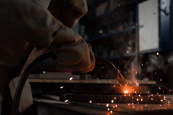 cropped shot of manufacture worker welding metal with sparks at factory 