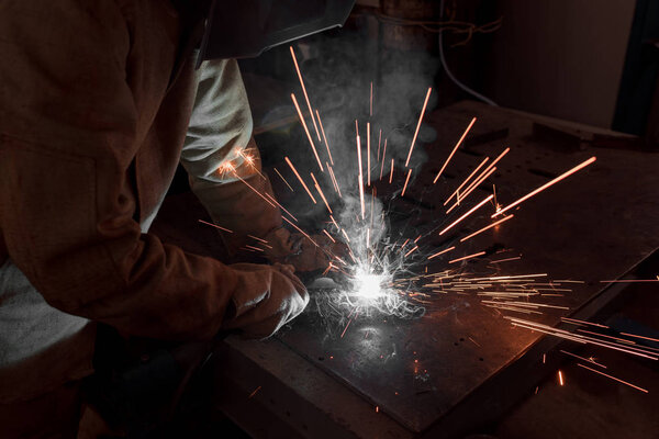 обрезанное изображение сварщика в защитной маске, работающей с металлом на заводе
 