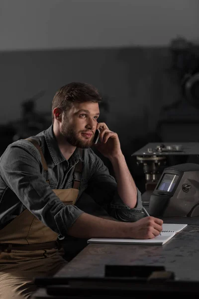 Young Workman Writing Textbook Talking Smartphone — Stock Photo, Image