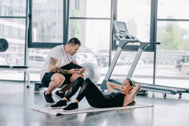 erkek kişisel antrenör zamanlayıcı ve atletik kadının spor salonunda fitness mat abs yapması ile