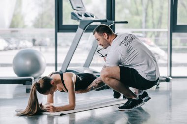 erkek kişisel antrenör genç atletik kadın tahta spor salonunda fitness mat yapmak için yardım