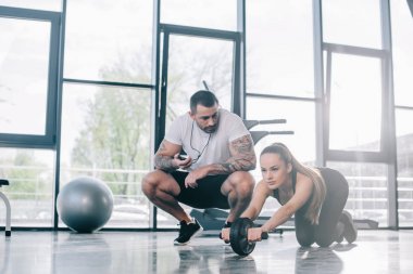 Zamanlayıcı ve genç sporcumuz abs rulo spor salonunda egzersiz yaparak ile oturan erkek kişisel antrenör